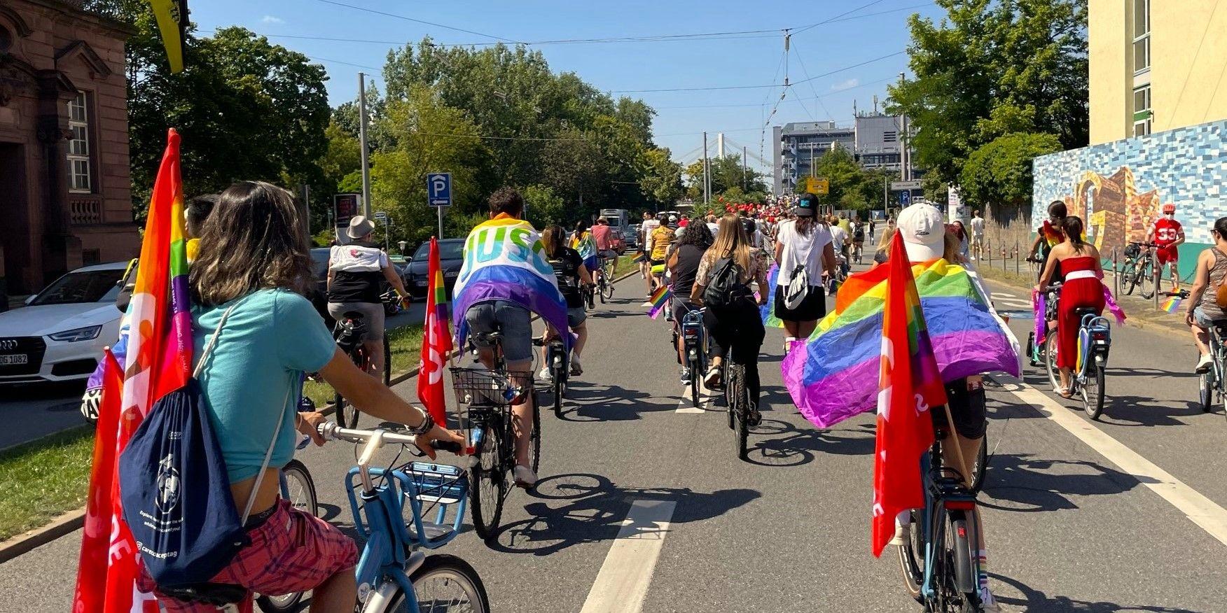 Raddemo bei Sonnenschein mit Pride-Flaggen an den Fahrrädern